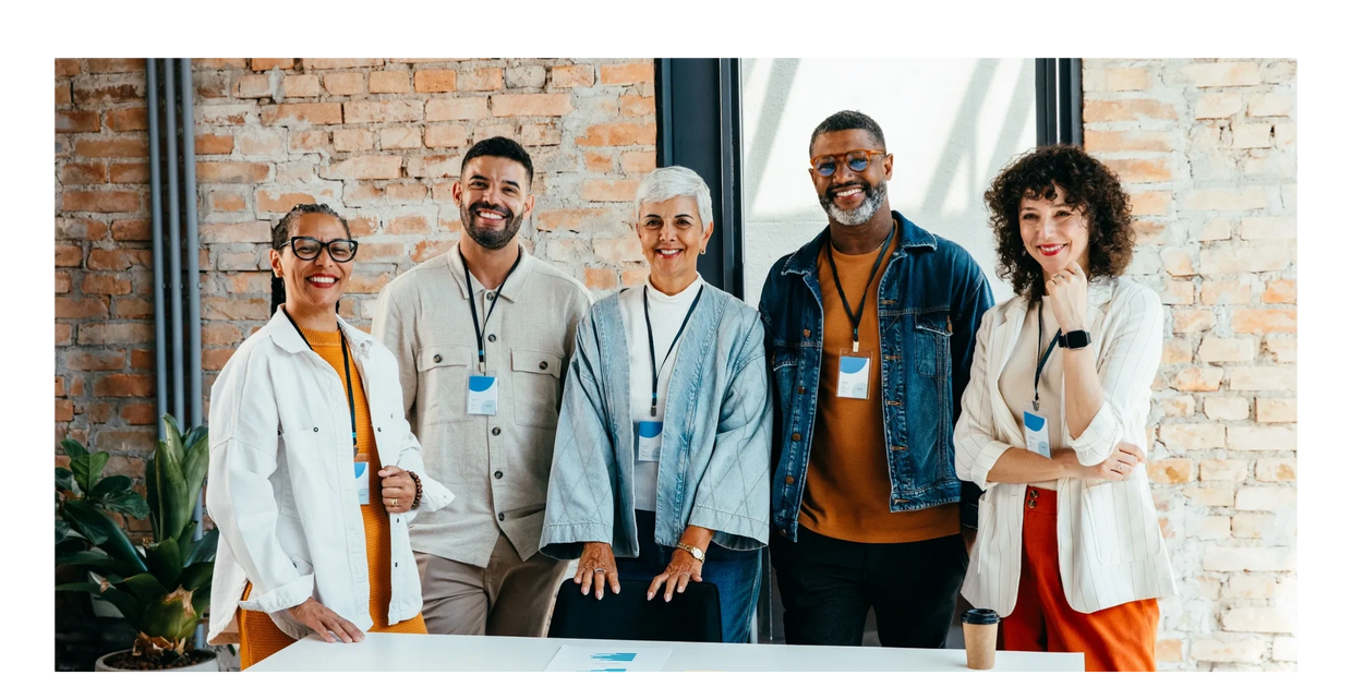 Diverse, smiling leaders standing in a modern office with brick walls. The group resembles values and resilience.