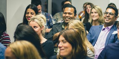 A group of diverse employees looking towards a speaker and laughing. 