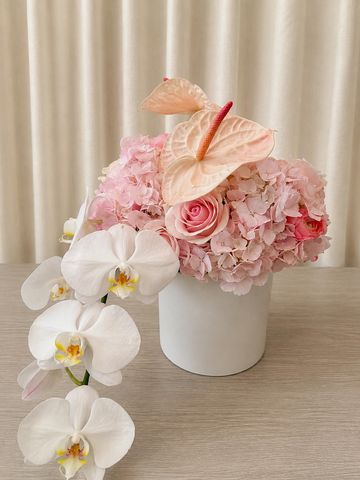 Elegant floral arrangement with white orchids and pink flowers in a white vase.