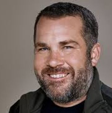 Smiling man with a beard and short hair in casual attire.