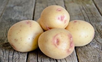 Four raw potatoes with slight red spots on a wooden surface.