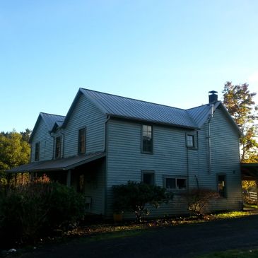Two-story house with a metal roof in a rural setting under clear skies.
