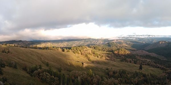 Sunlit rolling hills under a cloudy sky in a vast landscape.