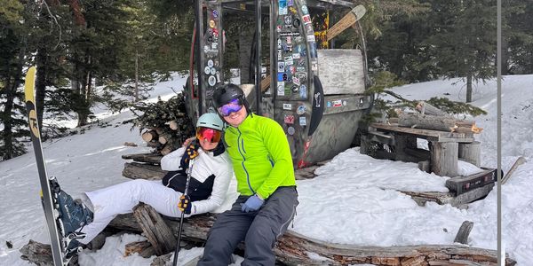 Two skiers resting in snowy forest near a gondola cabin.