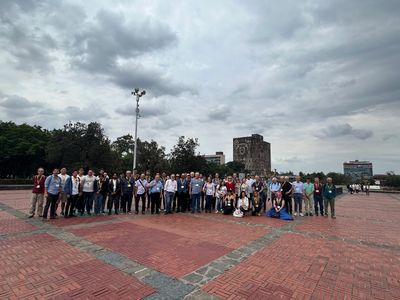 Large group posing outdoors on a cloudy day near historic tower.