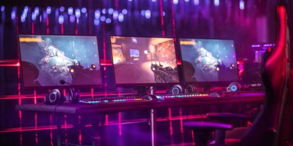 Three gaming monitors in a neon-lit room.