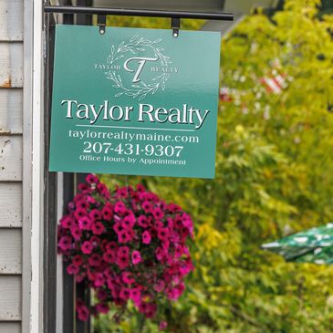 Taylor Realty sign with contact details and hanging flower basket.
