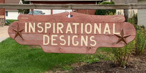 Wooden sign reading "Inspirational Designs" in front of a brick building.