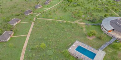 Aerial view of a resort with huts, a pool, and green landscape.