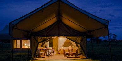 Cozy illuminated safari tent at dusk with seating inside.