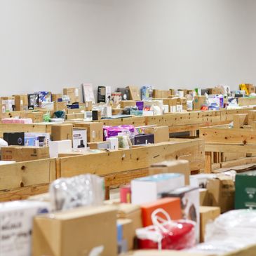 Rows of wooden tables filled with assorted boxed items in a warehouse.