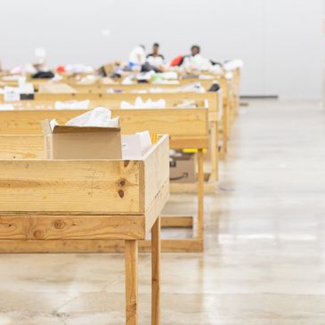 Empty wooden sorting tables in a large warehouse with a few people in the background.