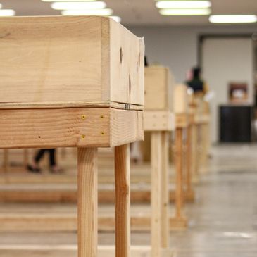 Rows of wooden tables lined up in a spacious room with bright overhead lights.