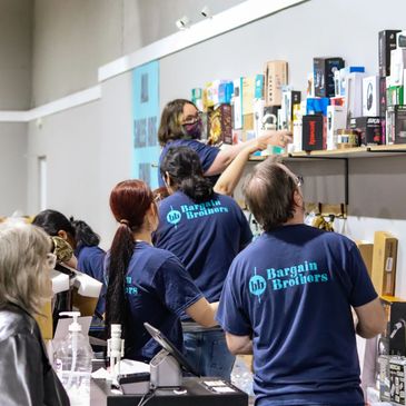 Team members in "Bargain Brothers" shirts organize products on shelves in a store.