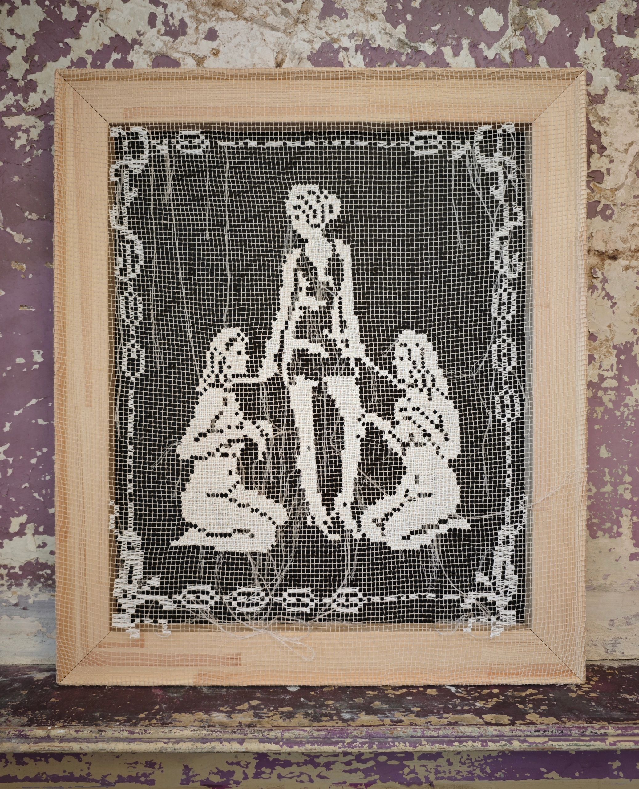 Framed lace artwork with human figures on worn purple surface.