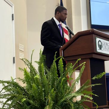 Man speaking at a podium in a formal setting.