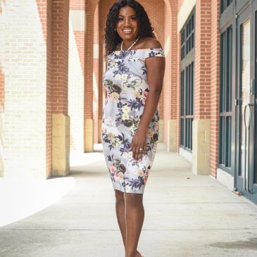 Woman in a floral off-shoulder dress smiling outdoors.
