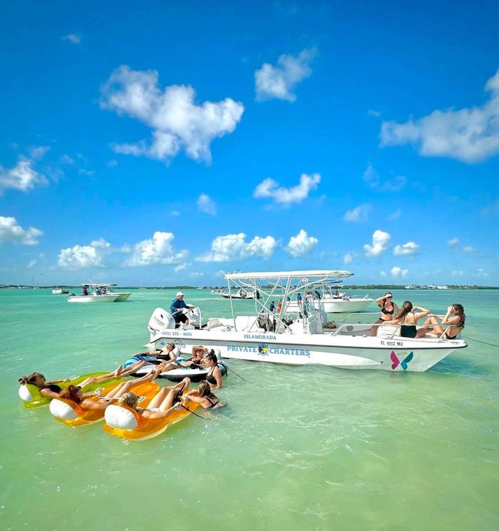 Group of people relaxing on floats and a boat in clear turquoise water under a sunny sky.