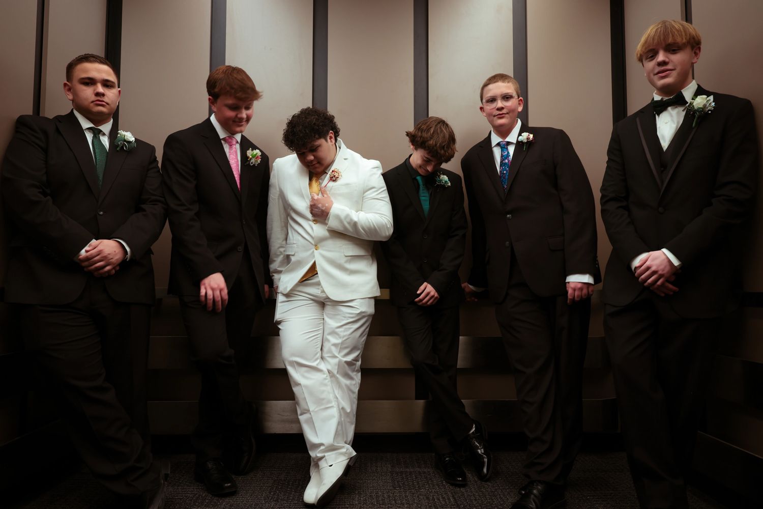 Group of young men dressed in formal suits, posing confidently indoors.