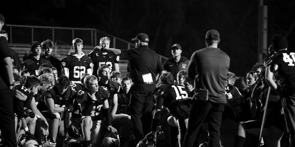 Football team huddling with coaches during a night game.