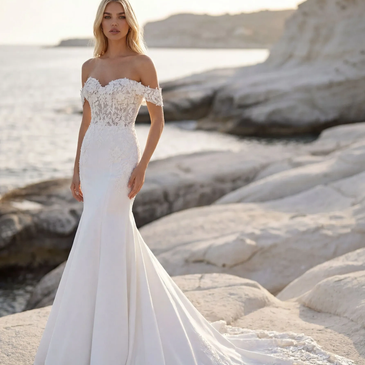 Woman in an elegant white wedding dress by the rocky shore.