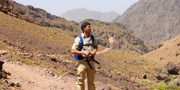A man hiking with a rifle in mountainous terrain.