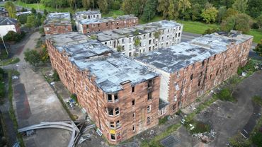 Aerial view of a large, abandoned brick building complex surrounded by greenery.