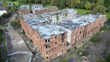Aerial view of a large, abandoned brick building complex surrounded by greenery.
