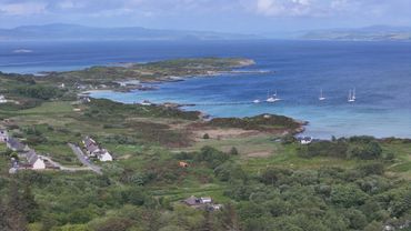 Scenic coastal landscape with green hills and boats on blue water.