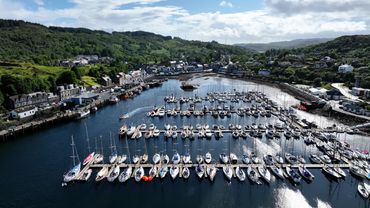 Aerial view of a marina filled with sailboats and surrounded by green hills and town buildings.