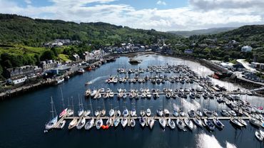 Aerial view of a marina filled with sailboats and surrounded by green hills and town buildings.
