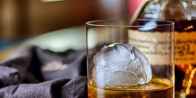 Whiskey glass with a large round ice cube on a cloth.