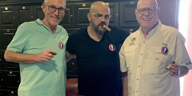 Three men enjoying cigars together, smiling and posing for the photo.