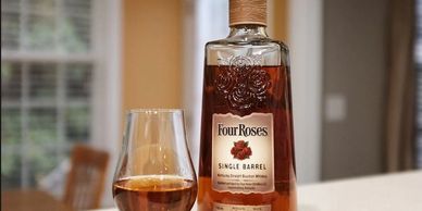 A bottle of Four Roses Single Barrel bourbon whiskey with a filled glass on a countertop.