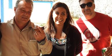 Three people posing together, one holding a cigar and another holding a drink can.