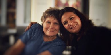 Two women smiling warmly and posing closely for a photo indoors.