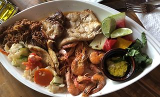 A plate with shrimp, grilled meat, vegetables, lime, and dipping sauce.