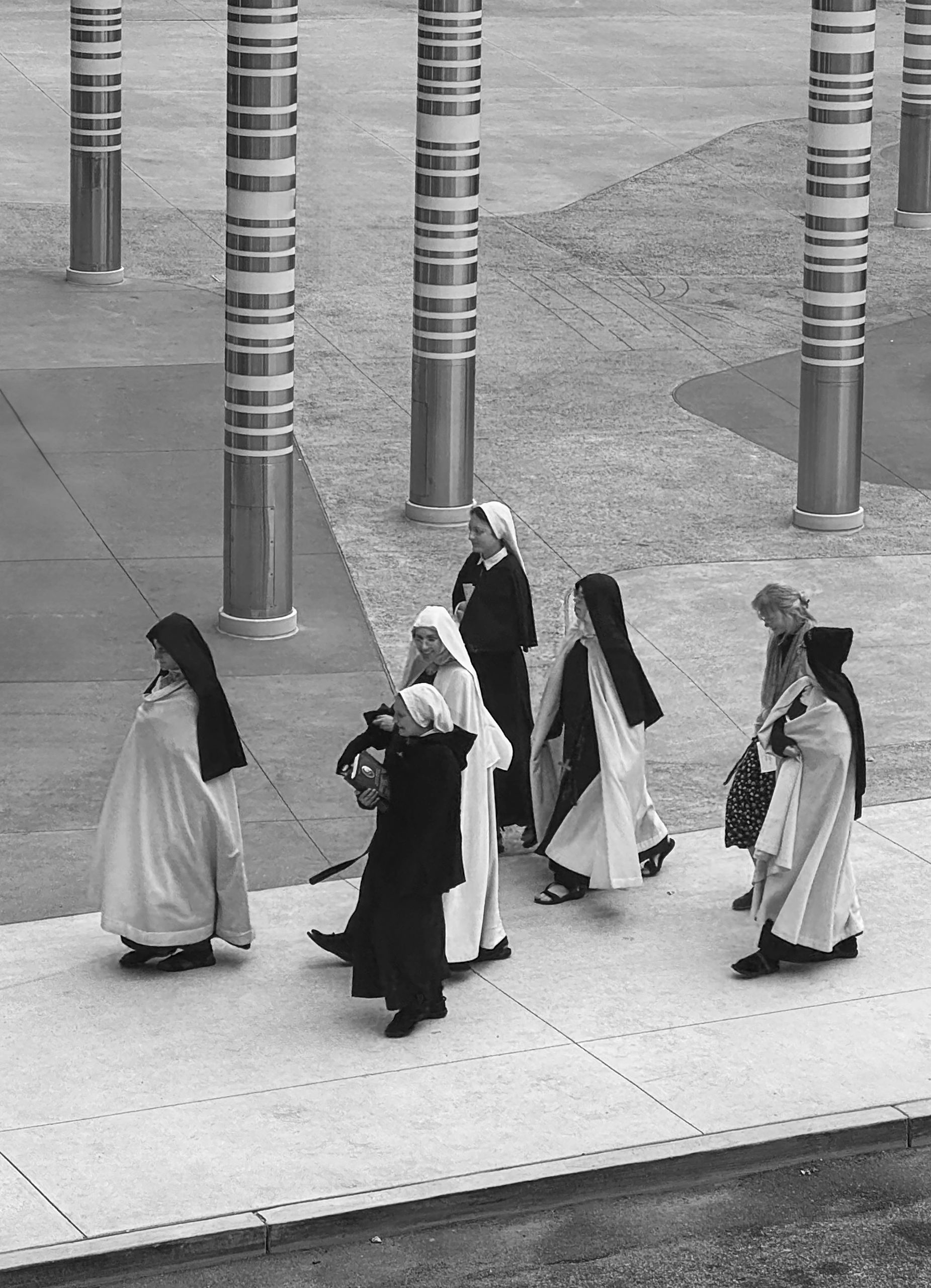 A group of nuns walking together outdoors near patterned pillars.