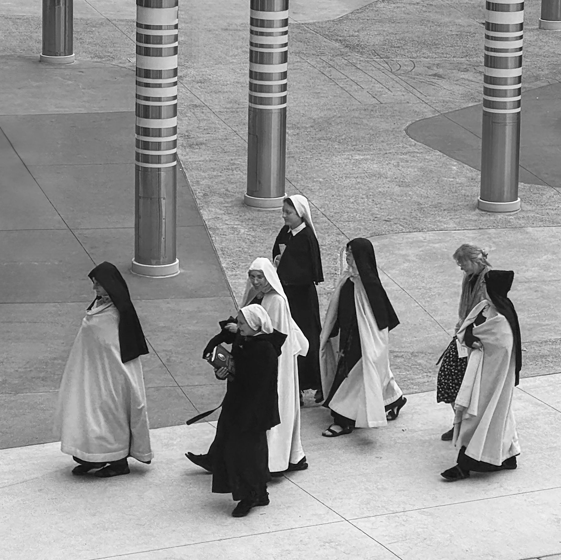 A group of nuns walking together outdoors near patterned pillars.