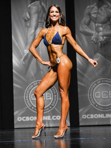 Female bodybuilder posing on stage in blue bikini.