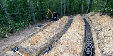 Excavated trenches with drainage pipes in a wooded area.