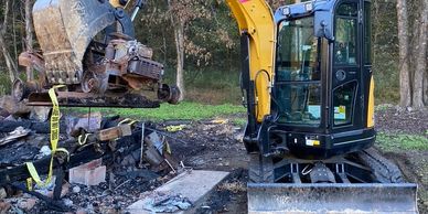 Excavator at a burnt site with debris and caution tape around.