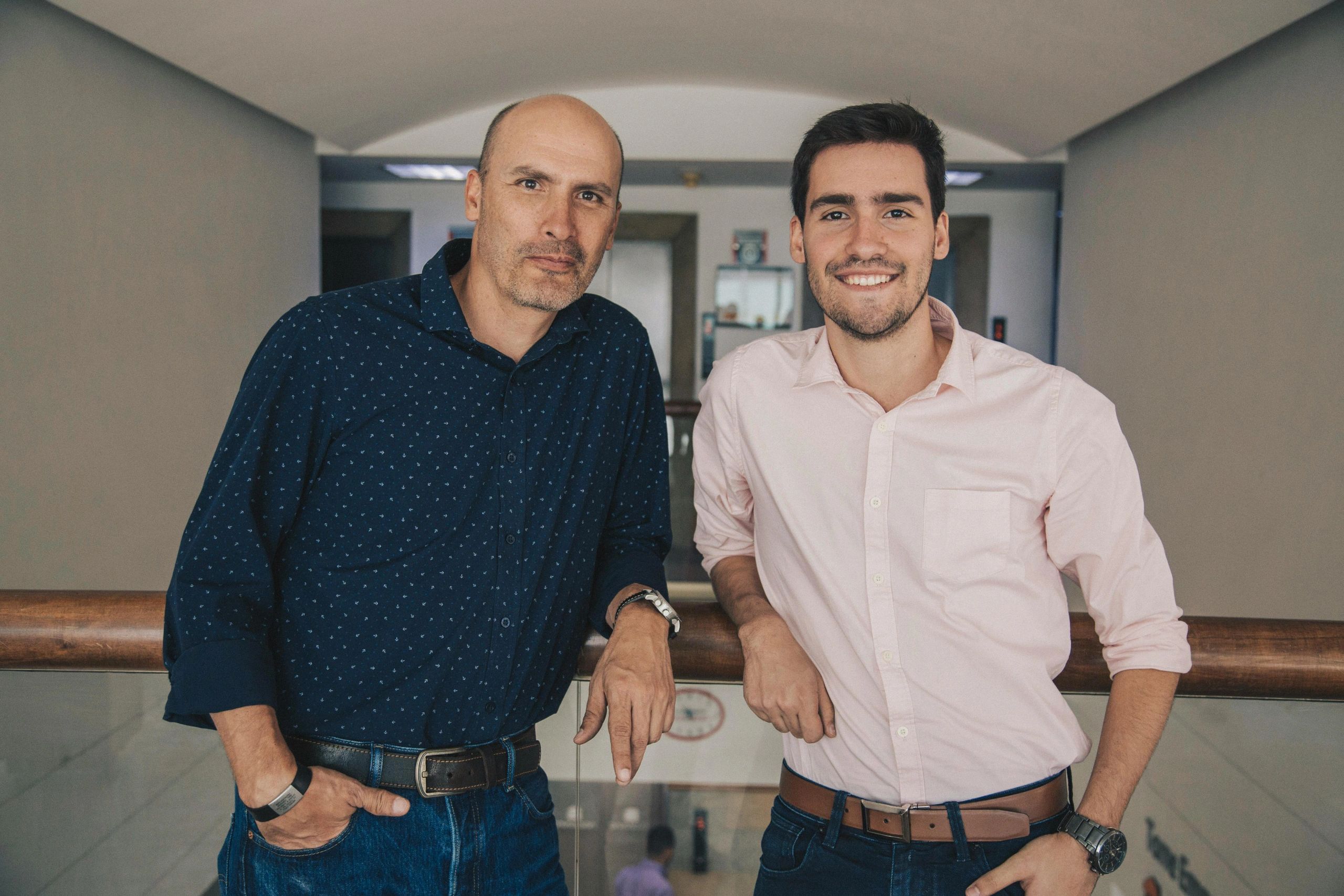 Two men posing casually indoors, one smiling and one serious.