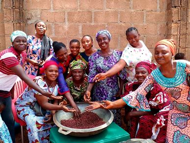 A group of women happily gathering around a large bowl of beans.