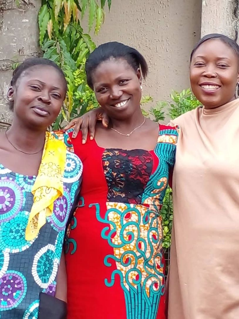 Three smiling women standing together outdoors in colorful attire.