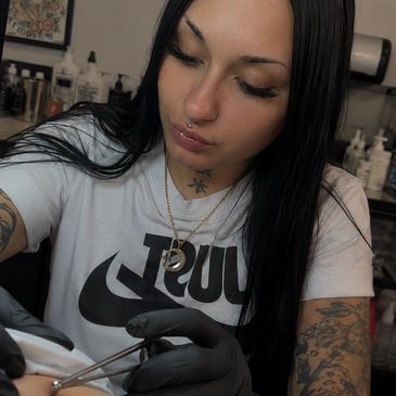 A woman with tattoos and piercings working with tweezers.