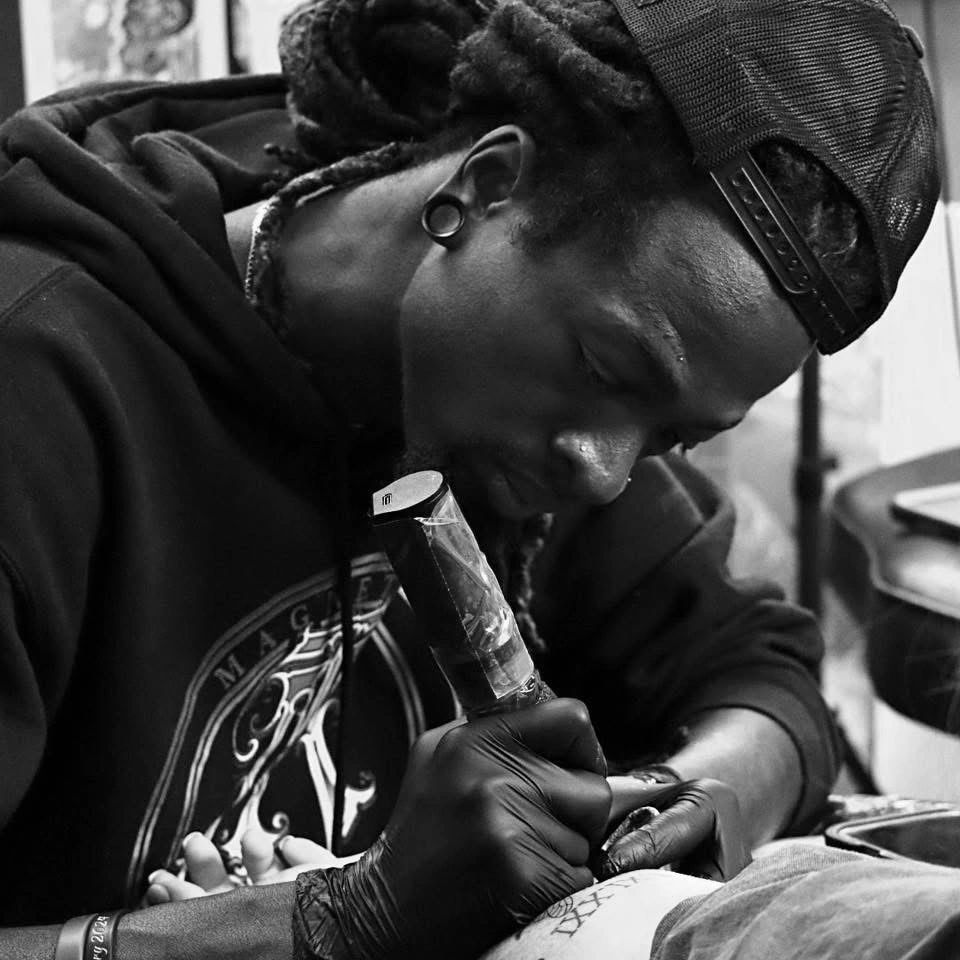Man tattooing a client's leg in a focused black-and-white shot.