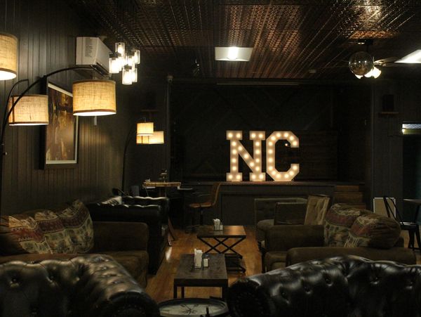 Cozy dimly lit lounge with vintage furniture and illuminated NC sign.