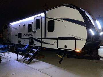 RV camper illuminated at night with chairs outside.