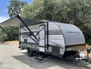 Compact RV trailer with extended awning parked outdoors.